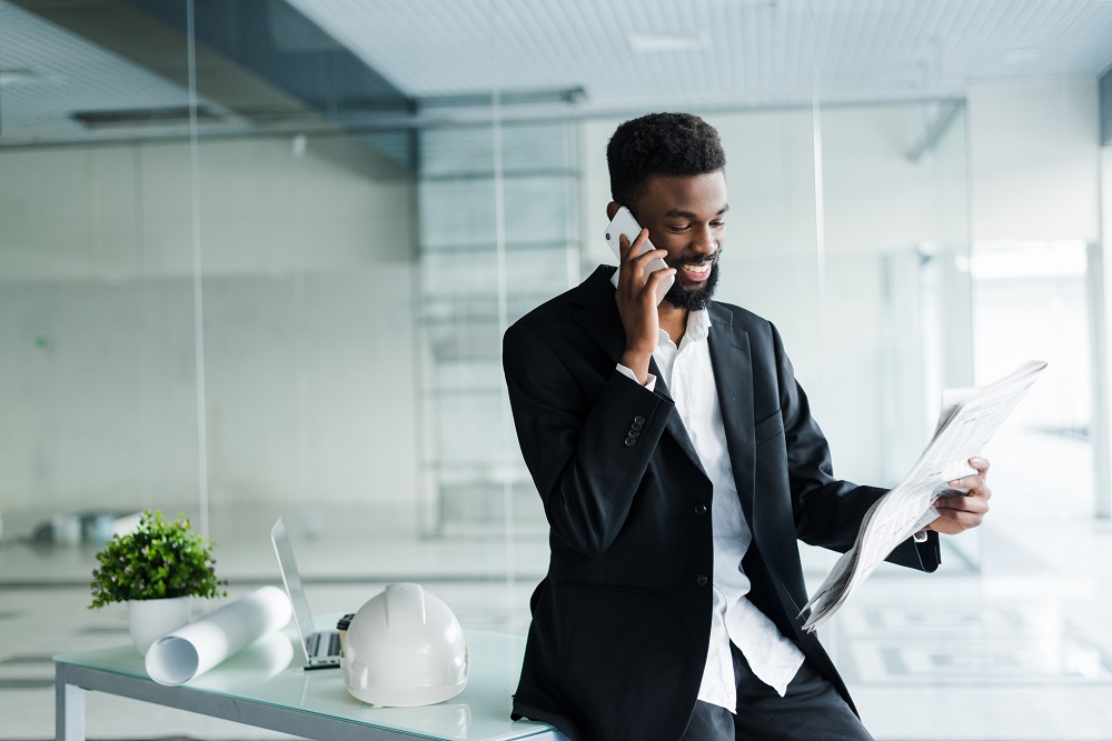 young african american businessman reading newspaper and talking on the phone in his office